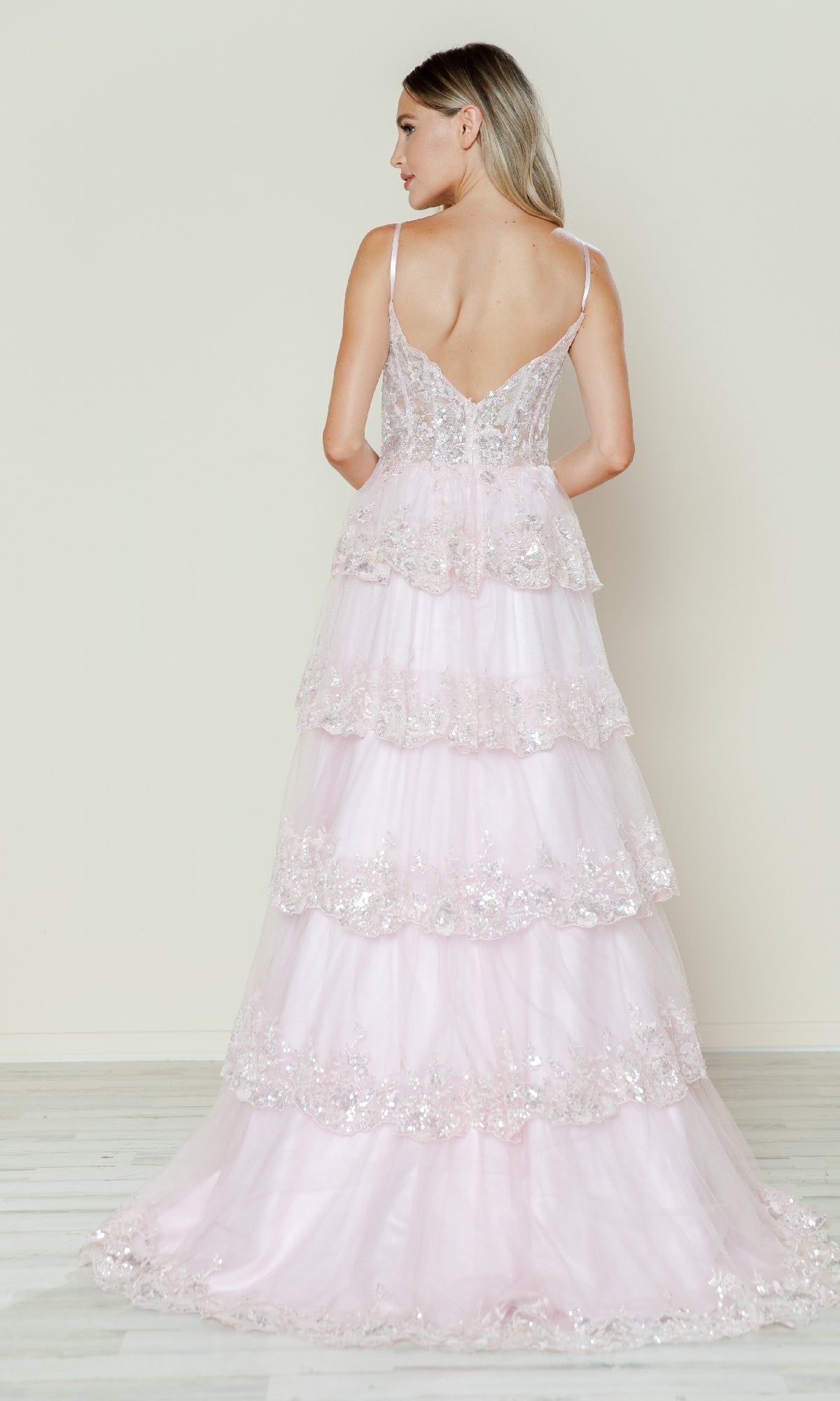Woman wearing the Long Glitter-Lace Tiered Prom Dress (Poly USA 9548), a light pink, floor-length gown with sequin embellishments, stands with her back to the camera against a plain background.
